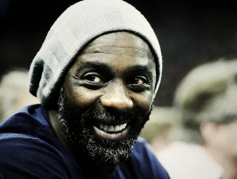 Idris Elba in a grey beanie, laughing