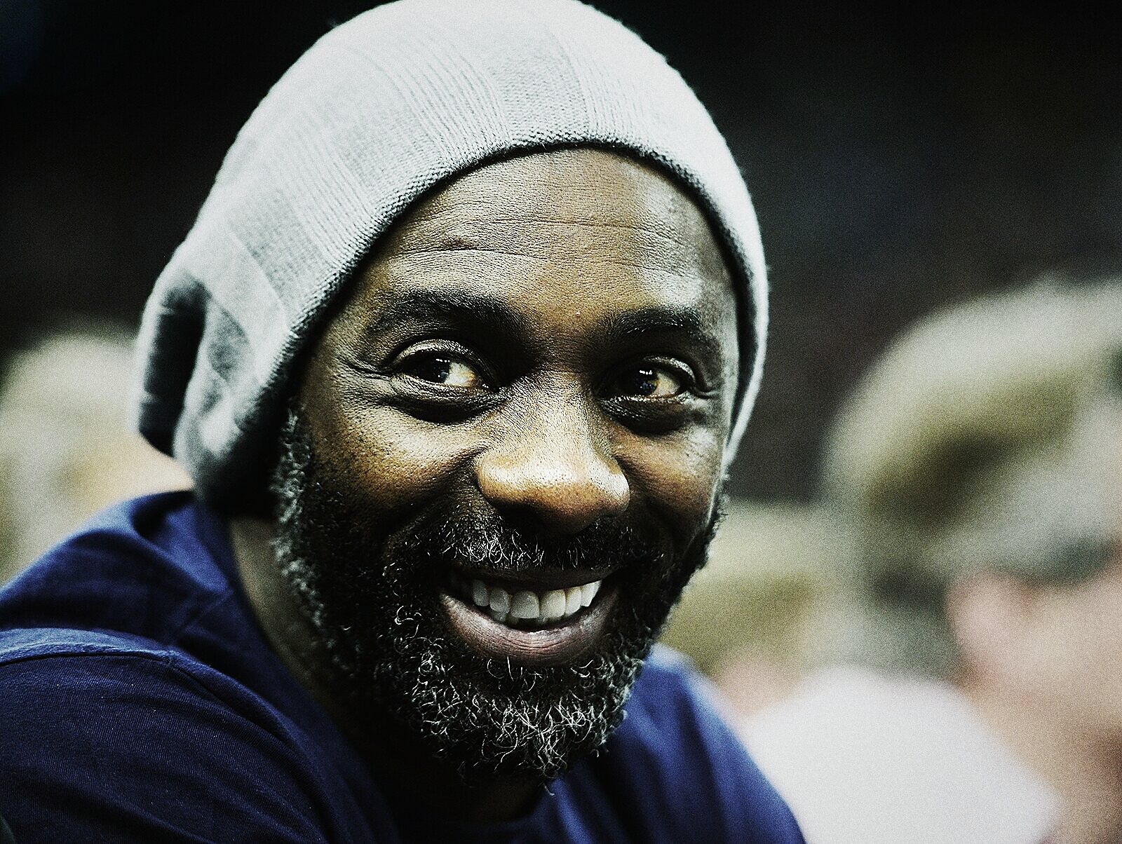 Idris Elba in a grey beanie, laughing